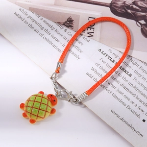Detail of green and red turtle charm with bright orange woven rope on a magazine page