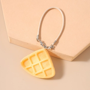 Macro detail of a realistic resin waffle charm with beige woven strap and silver clasp