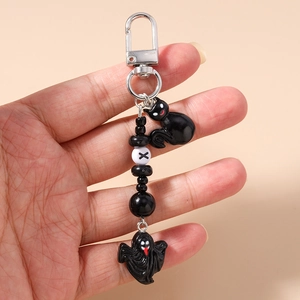 Detail of beaded Halloween keychain with black cat and ghost charms held in hand