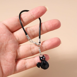 Detail of a black cat charm with silver lobster clasp and woven cord held in hand