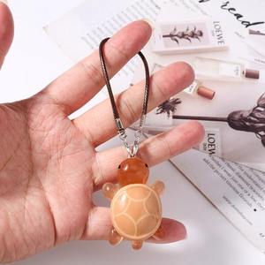 Close-up of a cute amber resin turtle charm with silver metal clasp and brown cord
