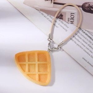 Detailed view of yellow waffle charm with silver lobster clasp and beige braided lanyard
