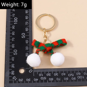 Macro detail of Christmas bow keychain with red-green stripes and white pom-poms on ruler