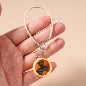 Detailed view of handmade dumpling steamer pendant with woven cord on a mobile strap