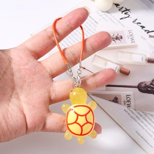 Detailed view of a cute yellow resin turtle charm with orange woven strap and metal clip