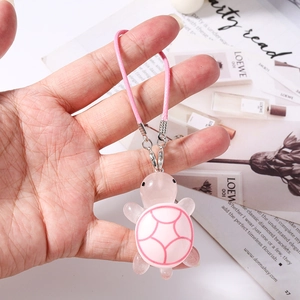 Detail of pink resin turtle charm with woven strap and metal lobster clasp held in hand