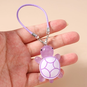 Macro detail of a cute purple resin turtle charm held in hand with woven strap