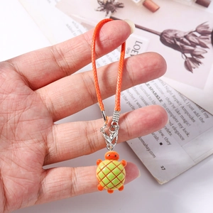 Close-up of a green plaid turtle charm with an orange braided cord and silver clasp