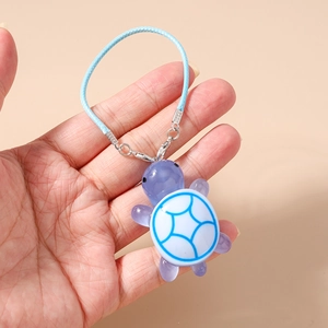 Close-up of a purple resin turtle charm with blue woven cord on a soft background