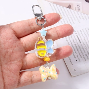 Detail showing cartoon bee keychain with blue star and yellow bow charm held by hand