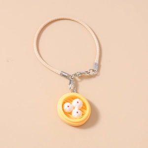 Macro detail of creative mini dumpling steamer charm on a beige braided strap