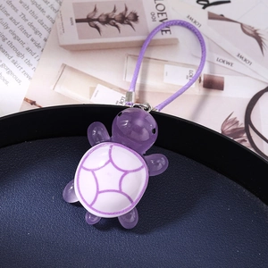 Detailed view of a purple resin turtle charm with woven strap on a dark blue tray