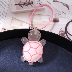 Close-up of cute pink resin turtle charm with woven strap on a dark display tray