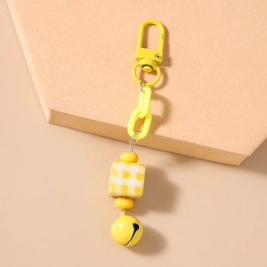 Detail of yellow chunky chain keychain with square bead and small bell on warm background