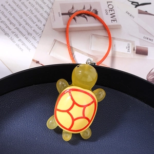 Macro detail of a yellow resin turtle charm with red geometric shell patterns and cord
