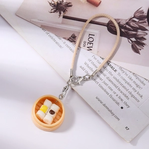 Close-up of a realistic mini dim sum steamer pendant with woven beige strap and metal clasp