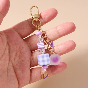 Detail of a purple beaded keychain with a checkered cube and letter V pendant