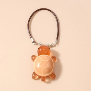 Detail of orange translucent turtle charm with beige patterned shell and woven strap