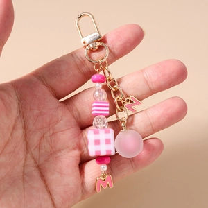 Detailed view of pink beaded keychain with geometric charms held in hand for scale