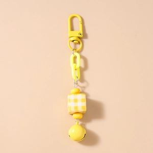 Close-up of yellow checkered cube bead and small bell on a stylish chain keychain