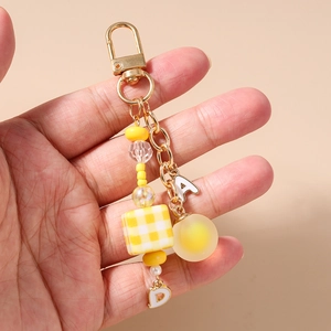 Handheld view of yellow beaded keychain with golden alloy clasp and letter charms