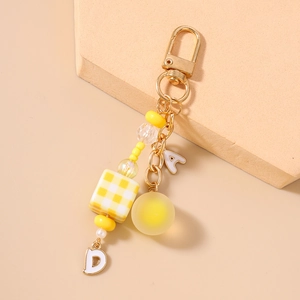 Detail of yellow checkered cube and letter charms on a golden beaded keychain