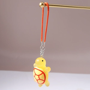 Detail of cute yellow transparent turtle charm with red grid pattern and orange lanyard