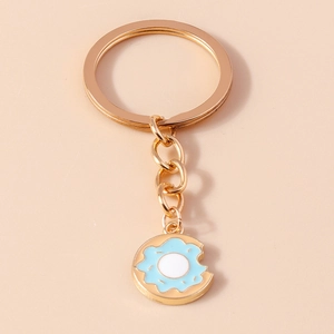 Dettaglio del portachiavi a ciambella blu morsicata con anello dorato su sfondo beige