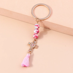 Beaded tassel keychain with golden cross and evil eye charm on soft apricot background