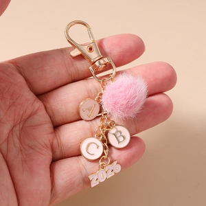 Dettaglio del portachiavi con pompon rosa, lettere ABC dorate e ciondolo anno 2026