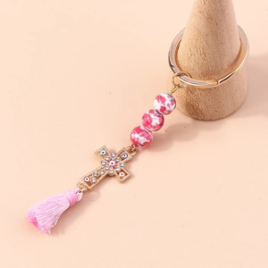 Pink beaded keychain with evil eye cross pendant and tassel decoration on wood