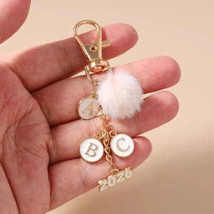 Dettaglio portachiavi pompon rosa con ciondolo dorato 2026 e lettere dell'alfabeto A, B, C