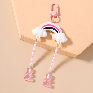 Detail of rainbow keychain with pink bear pendants and white clouds on beige stand