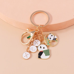 Golden panda keychain with bamboo charm and lettered enamel tags on pink display