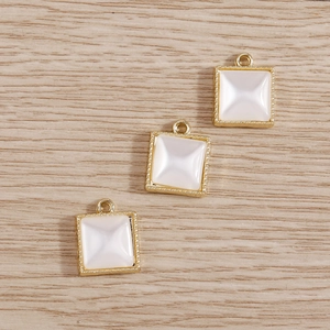 Close-up of square pearl charms with gold beaded edges and pyramid faceted inlay
