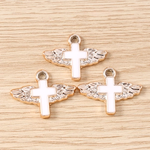 Three rose gold wing cross pendants with white enamel on a light wooden background