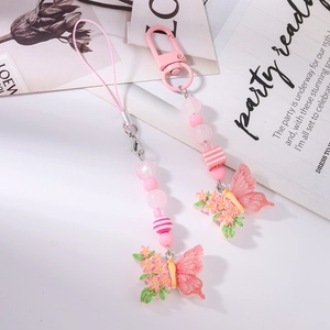 Detailed view of pink beaded phone charm with butterfly and flower pendants on a magazine