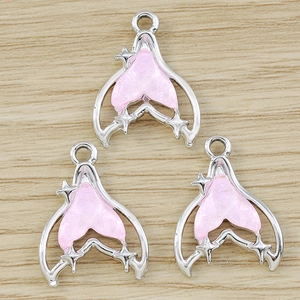 Three silver alloy fish tail pendants with pink enamel and star charms on wood