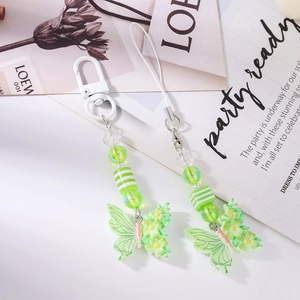 Detail of green butterfly beaded phone charms with flower accents on white desktop