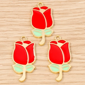 Macro shot of three red enamel rose flower charms with gold plating on wooden background