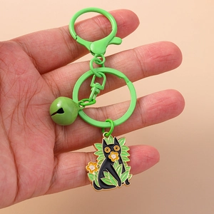 Detail of a cute black cat enamel keychain with green leaves and a small golden bell