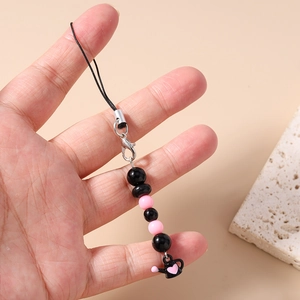 Détail du bijou de téléphone perlé rose et noir avec un pendentif arrosoir et cœur