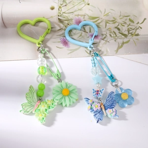 Détail d'un porte-clés perlé avec breloques papillon et marguerite sur fond blanc épuré