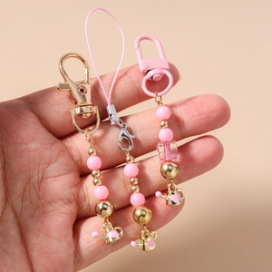 Pink beaded phone charm with heart kettle pendant held in hand for size reference