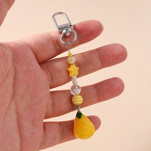 Detail of yellow star beaded keychain with lemon pear charm held in hand on neutral backdrop
