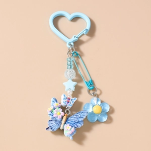 Détail d'un porte-clés perlé bleu clair avec breloques marguerite, papillon et perles d'étoiles