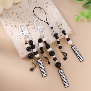 Musical theme phone strap with black and white beads and piano key charms on marble surface