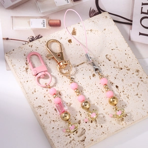 Pink beaded phone charm strap and heart kettle keychain set on aesthetic stone background