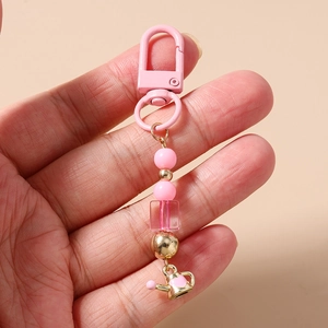 Close-up of pink beaded keychain with a gold heart pattern kettle pendant on hand