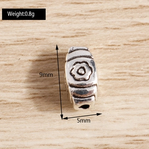 Detailed macro of a floral engraved silver spacer bead showing 9mm length and 0.8g weight